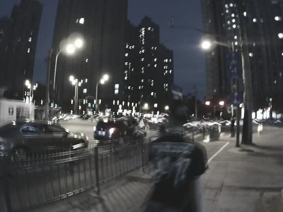 Verschwommene Nachtstraßenszene in der Stadt mit beleuchteten Gebäuden und fahrenden Fahrzeugen.